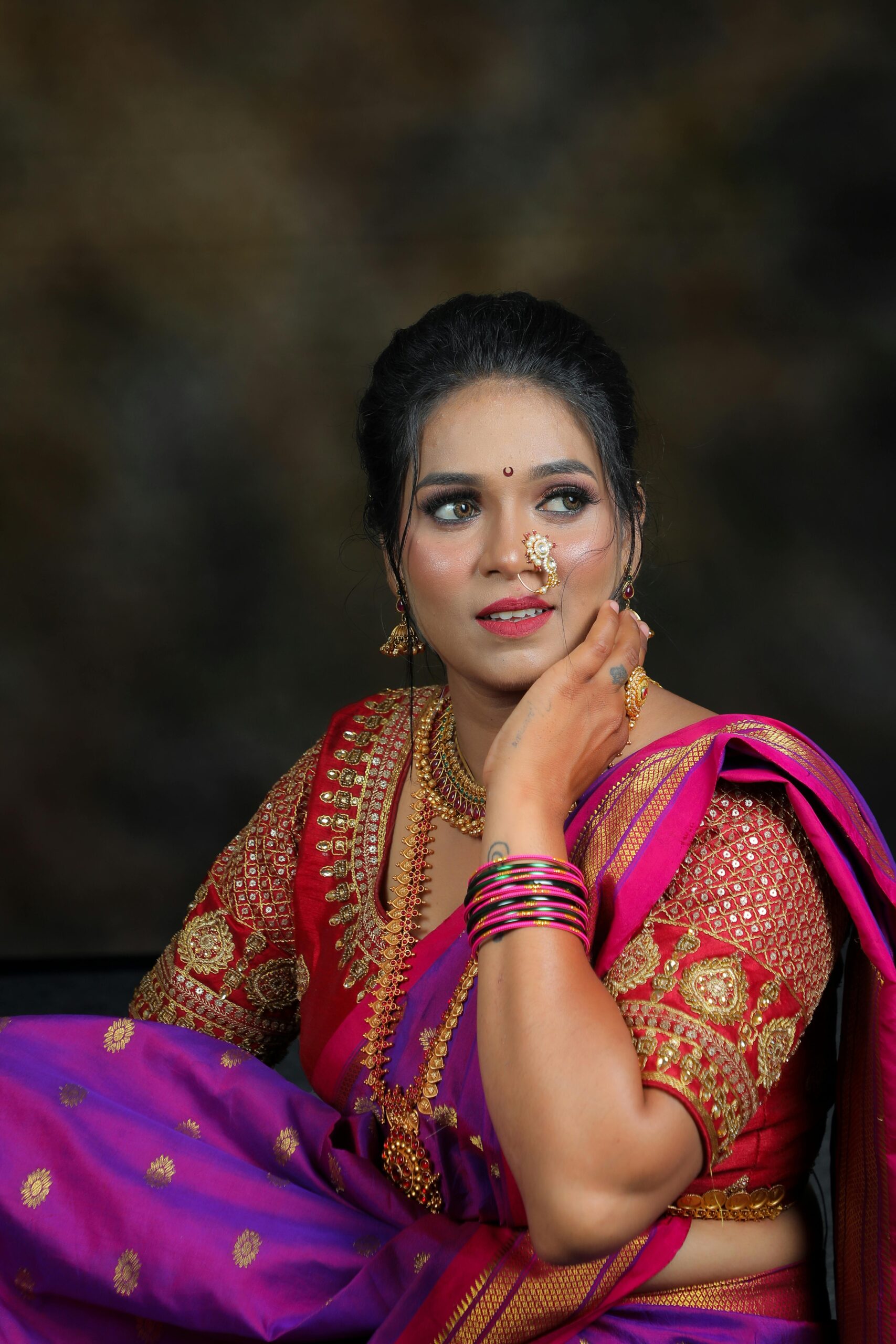 A woman wearing colorful traditional Indian attire adorned with jewelry, posing in a studio.