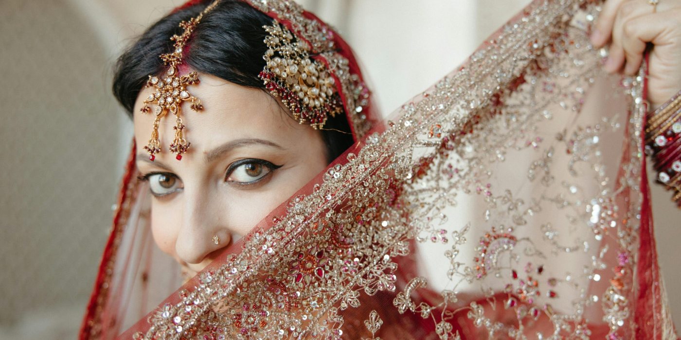 A traditional Indian bride with intricate jewelry and a shimmering red veil, displaying cultural elegance.